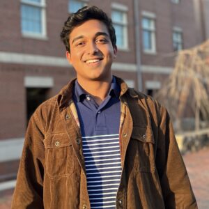 Shaurik Deshpande standing on UNC campus with a brown jacket on