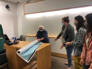 Professor Willis unrolling the Climatopia fabric next to two students.