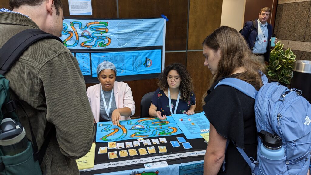 two Climatopia students showing two people the rules, cards, and game board of Climatopia.
