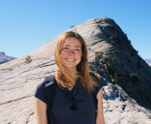 Lauren Cmiel standing on a mountain with a backpack on, on a sunny day