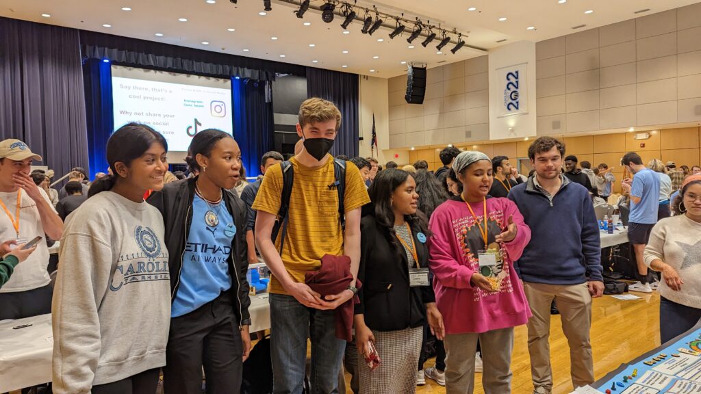 Group of students stand next to eachother while looking at Climatopia showcase at Makerfest