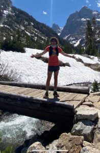 Jackson Krider in shorts and a t-shirt on a bridge in front of snowy mountains
