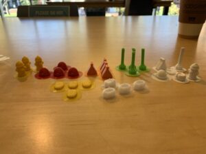 3d game pieces printed out in red, green, white, and yellow on a table
