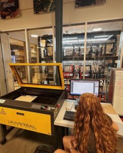 Student looking at computer while she operated a laser-wood cutting machine