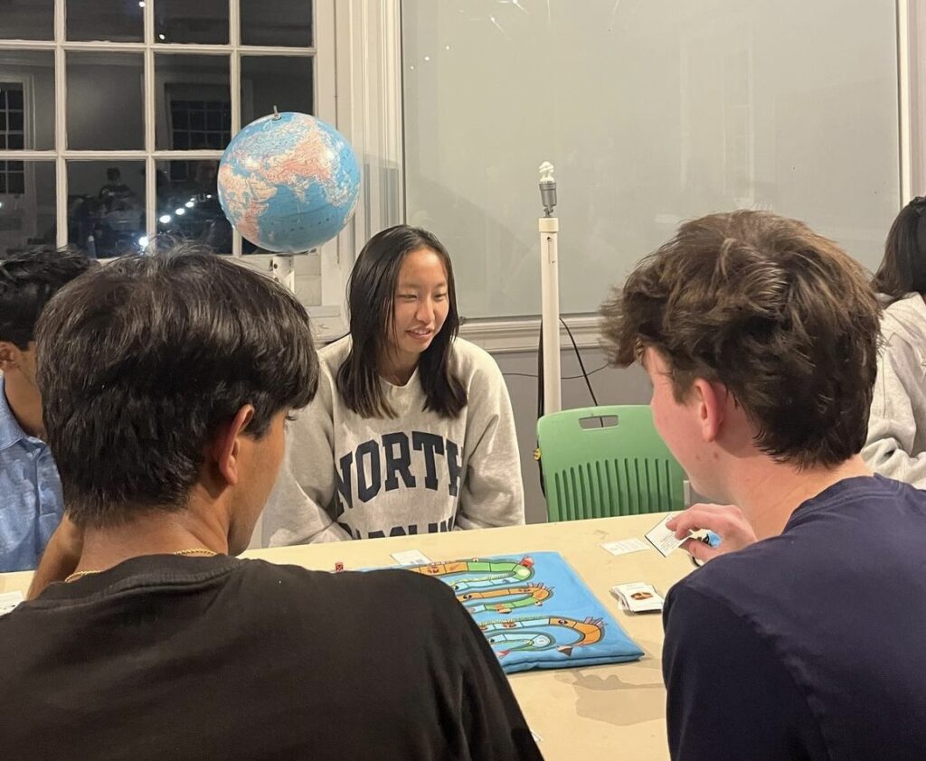 Student sitting behind climatopia game board in the background of two guys