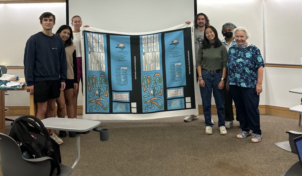 Group of Fall 2023 students holding up Climatopia fabric in the front of the class