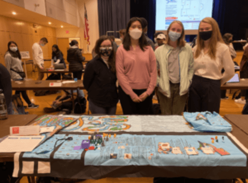 Group of Fall 2021 Climatopia makers standing behind their a table filled with Climatopia game board, game bags, and game cards at the Makerfest.