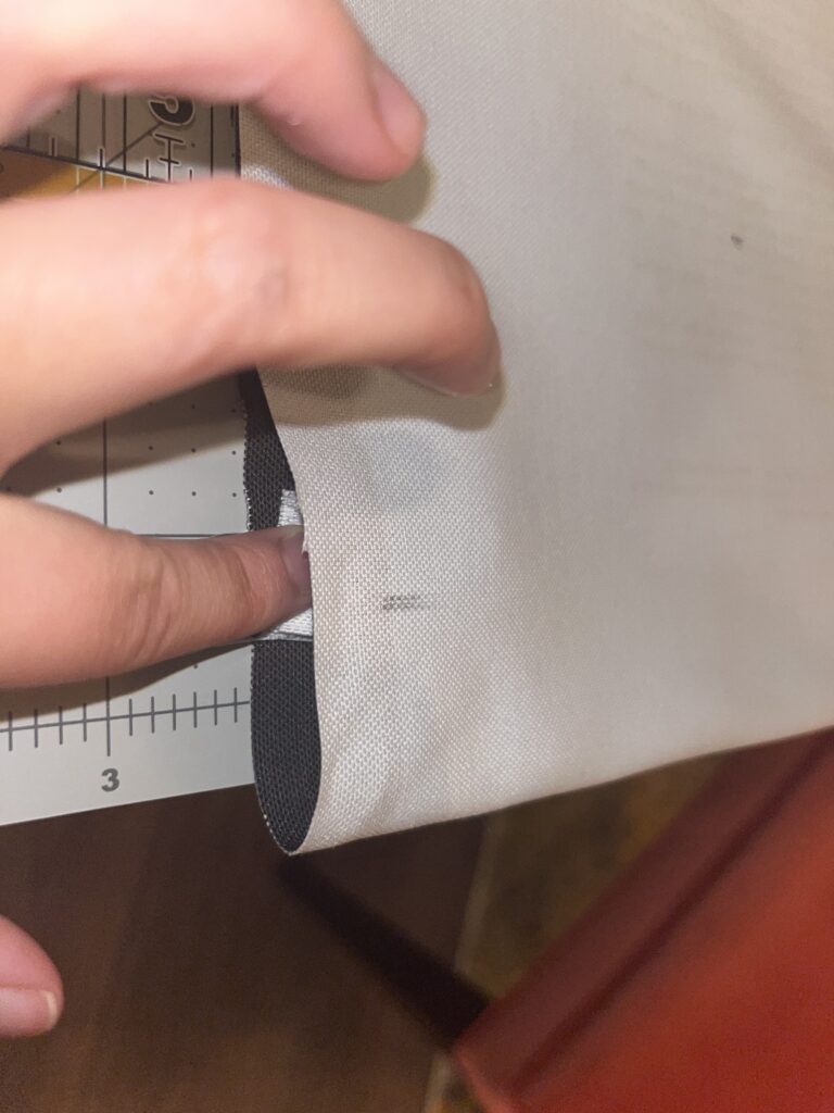 Pointer finger holding down white sewn tab between folded over fabric