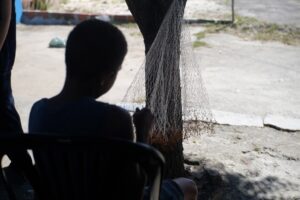 A shot from behind a boy who holds a fish net nera the shore