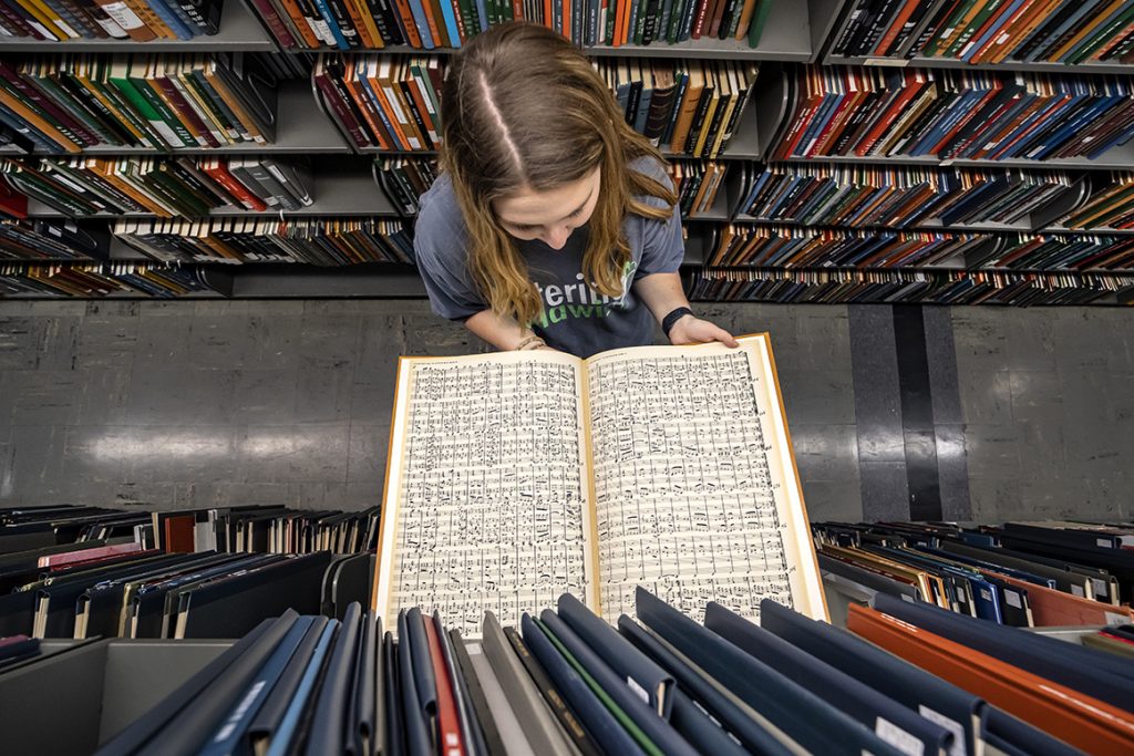 Girl looks at open score in the stacks of the music library