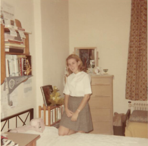 Marcia Citron poses with one knee on her bed, smiling at the camera, in her dorm room.