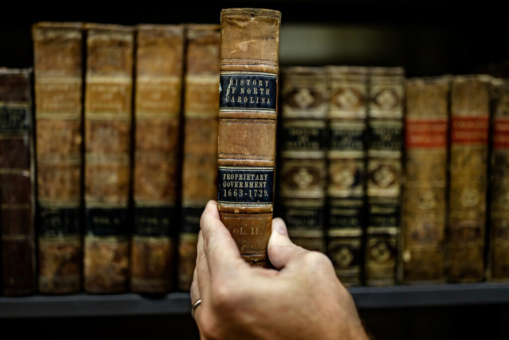 A hand removes a book from a shelf in the special collections area of Wilson Library.