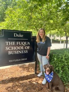 Courtney stands by the Fuqua School of Business sign with her dog.