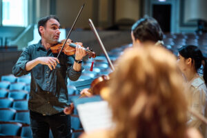 Nicholas DiEugenio demonstrates on his violin for students in Moeser Auditorium.