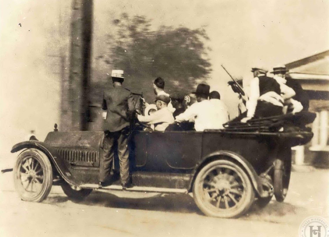A group of Caucasian men in a car during the 1921 Tulsa Race Massacre. One man stands on the car's running board. One man at the rear carries a rifle or shotgun.