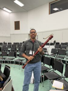 Samuel Edoho-Eket poses in a music classroom wearing jeans and a sweatshirt, bass recorder in-hand.