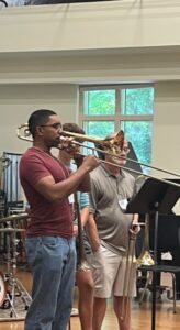 Samuel Edoho-Eket, wearing a red shirt and jeans, plays the trombone during the UNC Summer Jazz Workshop