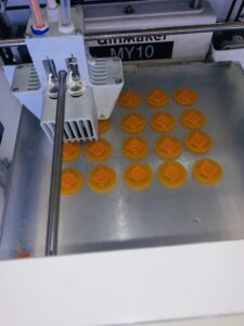 3D printer printing a batch of 20 orange fire hydrant game pieces